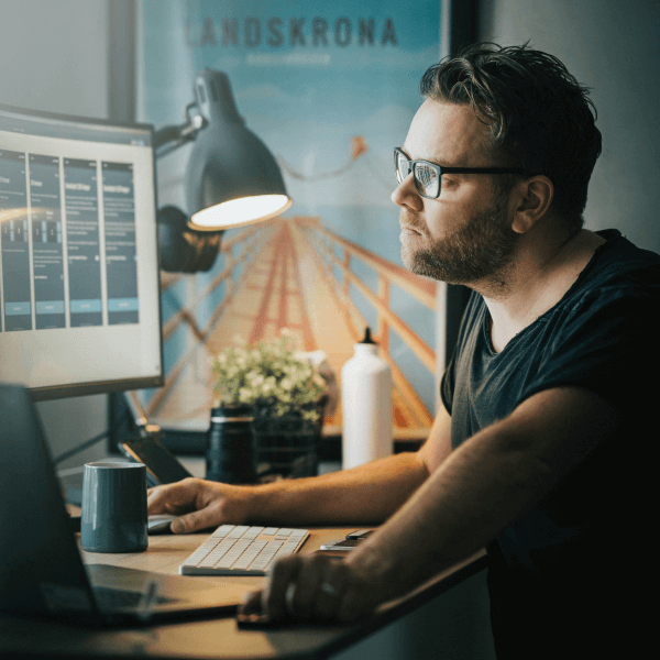 Man working at a desk, focused on computer screen displaying digital marketing analytics, with a coffee cup and plant nearby, in a modern workspace setting.