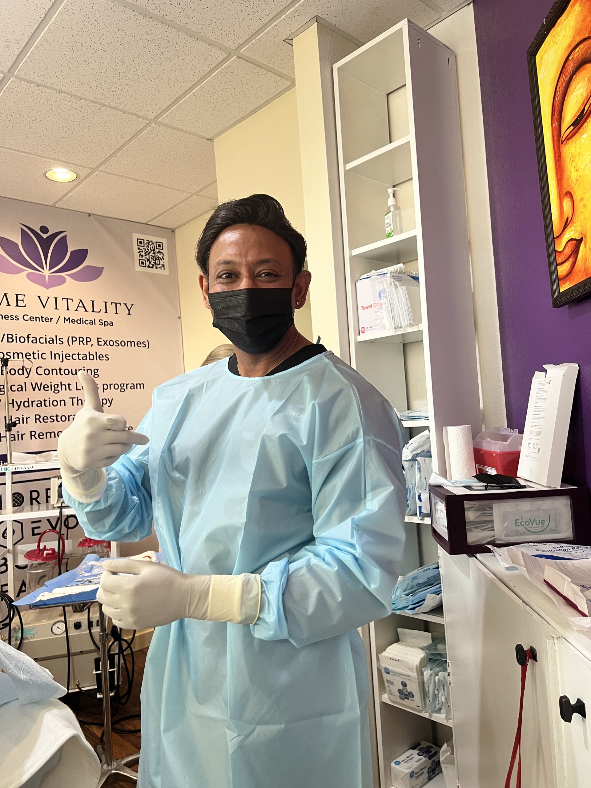 Medical professional in blue gown and gloves gesturing positively in Prime Vitality medical spa, showcasing patient-centered care and wellness services.