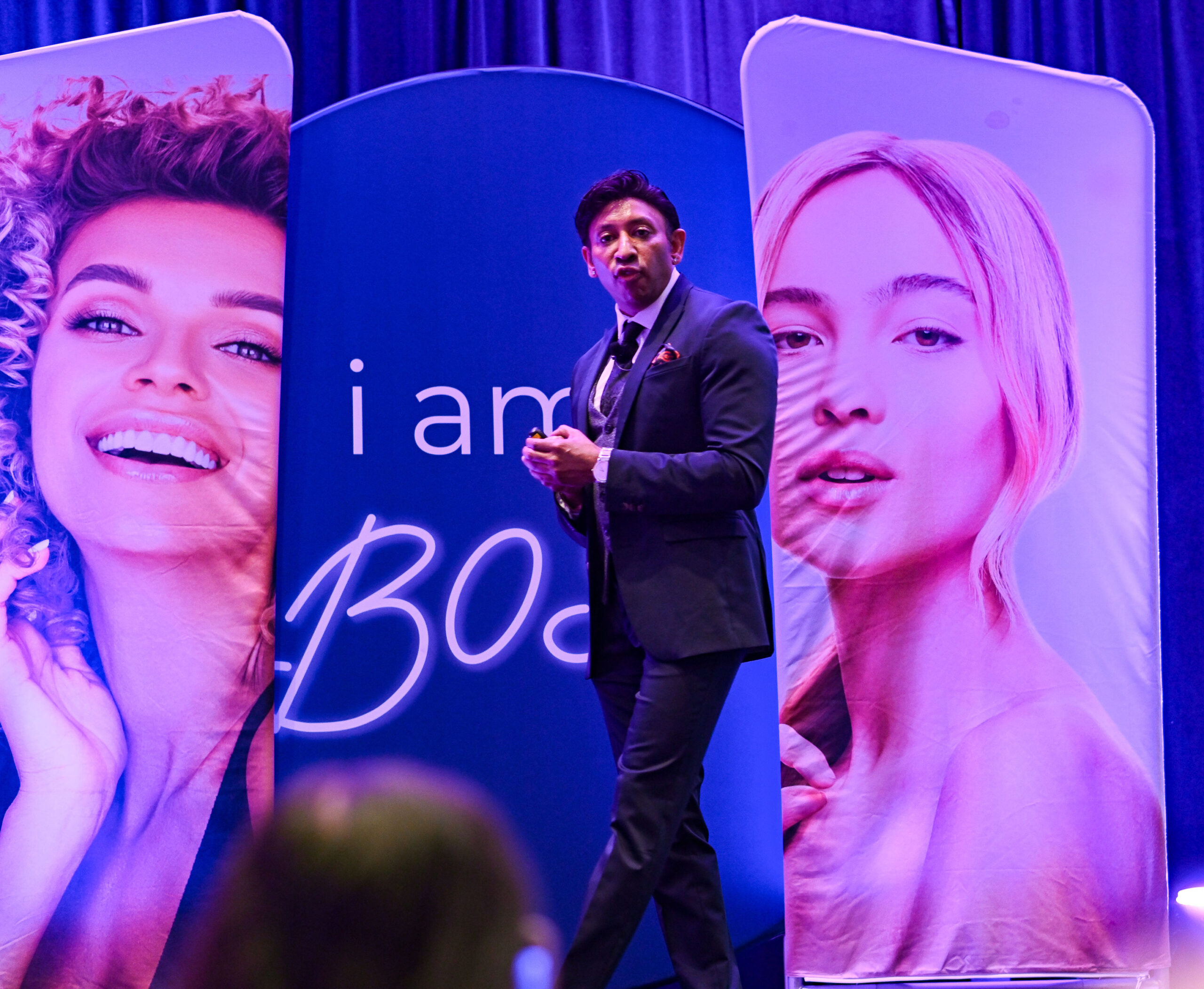 Dr. Goel presenting at the Beauty Boss conference, flanked by vibrant banners featuring smiling models, emphasizing aesthetic and regenerative medicine strategies.